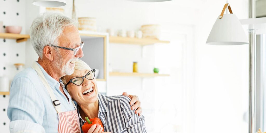 Happy elderly couple hugging and laughing together while enjoying each other's company in their kitchen.