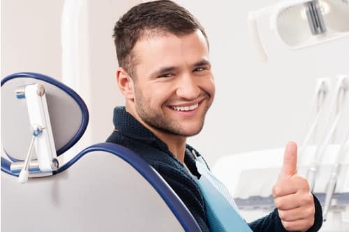 Man smiling and giving a thumbs-up in a dental chair, illustrating the positive impact of preventative orthodontic care for adults