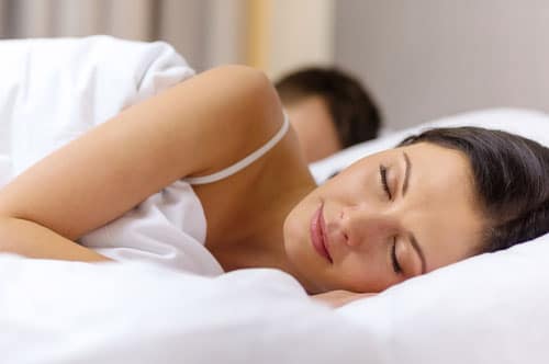 A woman peacefully sleeping in bed, eyes closed, embracing comfort amidst summer heat to combat sleep apnea