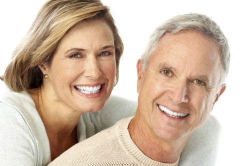 A cheerful couple with radiant smiles, illustrating the life-changing benefits of dental implants for their appearance