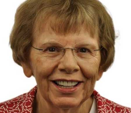 A senior dentist in a red shirt and glasses, showcasing a cheerful smile that highlights her teeth