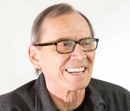 A dentist with glasses, dressed in a black shirt, showcases a cheerful smile that highlights his teeth, radiating positivity