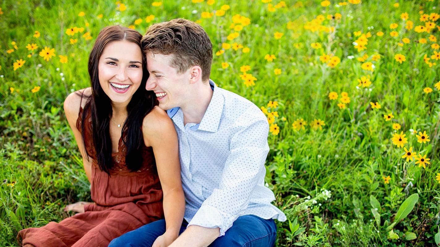 Happy couple smiling and enjoying a relaxing moment together in a green field with yellow flowers in bloom