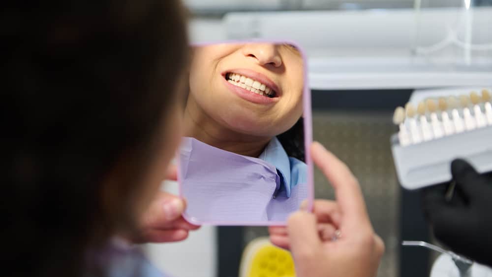 Woman examining her teeth in a mirror after receiving tooth-colored fillings, checking the results of her recent treatment