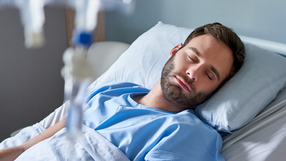 Man peacefully sleeping in a hospital bed, surrounded by medical equipment and soft lighting, representing a calm recovery after IV conscious sedation