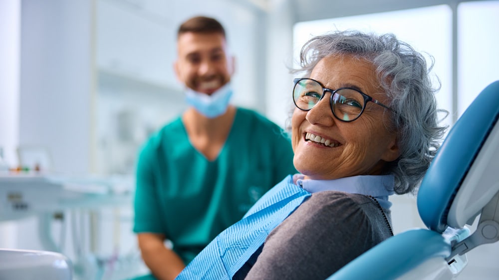 Smiling elderly woman in a dental chair, highlighting a positive experience with dental care and treatment, with a dentist in the background