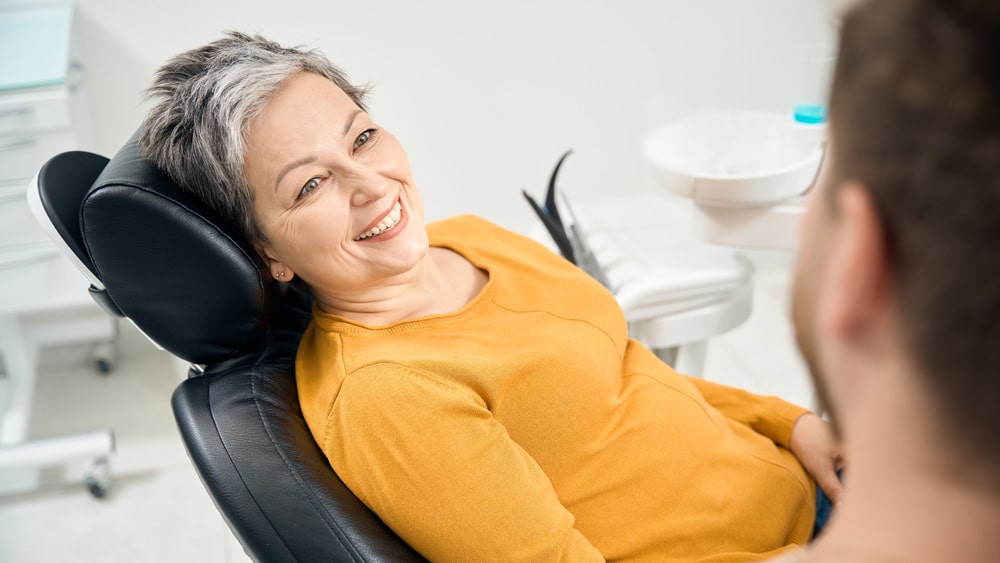 Woman in a yellow shirt sitting in a dental clinic chair, talking to her dentist about fluoride treatment in Stillwater, MN