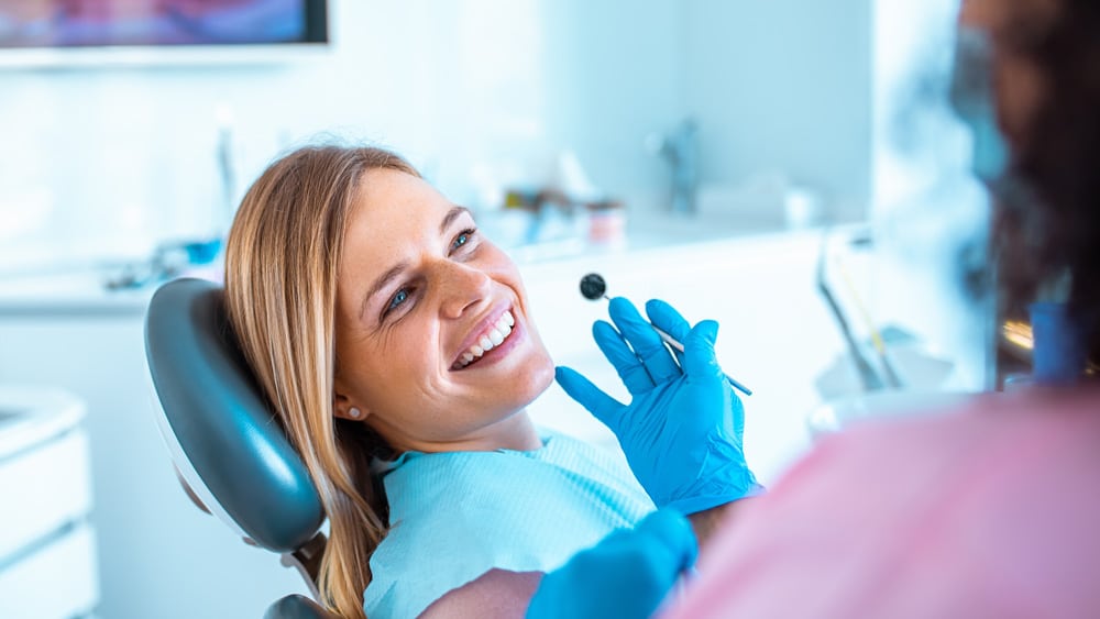 Woman in a blue shirt sitting in a dental chair, receiving routine dental cleaning from her dentist in Stillwater, MN