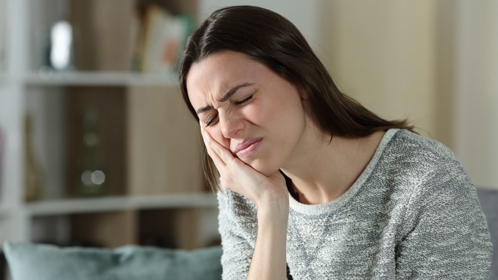 Woman experiencing toothache pain, holding her cheek in discomfort while touching the affected area