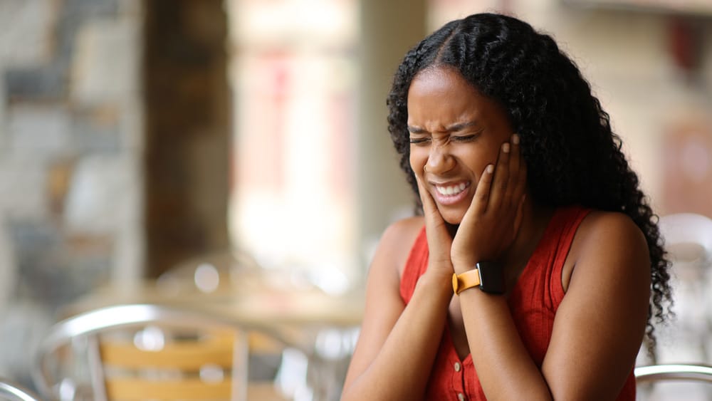 Woman in a red shirt experiencing toothache pain, holding her cheek in discomfort while touching the affected area